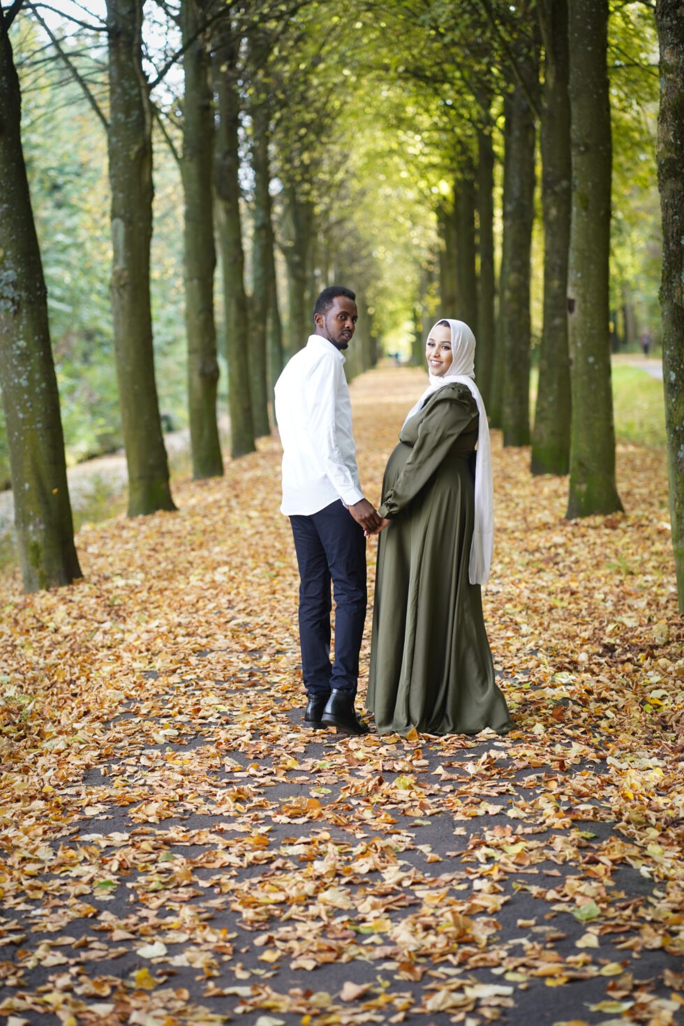 Een stel staat in een bosgebied in de herfst, met de vrouw in een groene jurk.