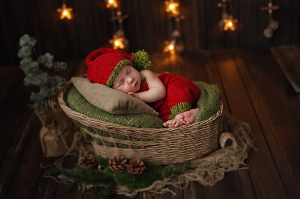 Pasgeboren baby in een feestelijke rood-groene outfit, slapend in een kerstmand met feestelijke decoraties.