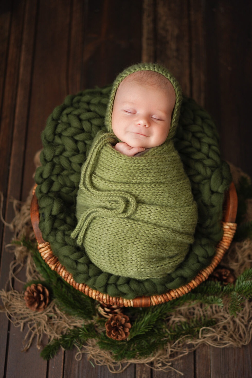 Pasgeboren baby in een donkergroene doek, slapend in een rustieke houten mand
