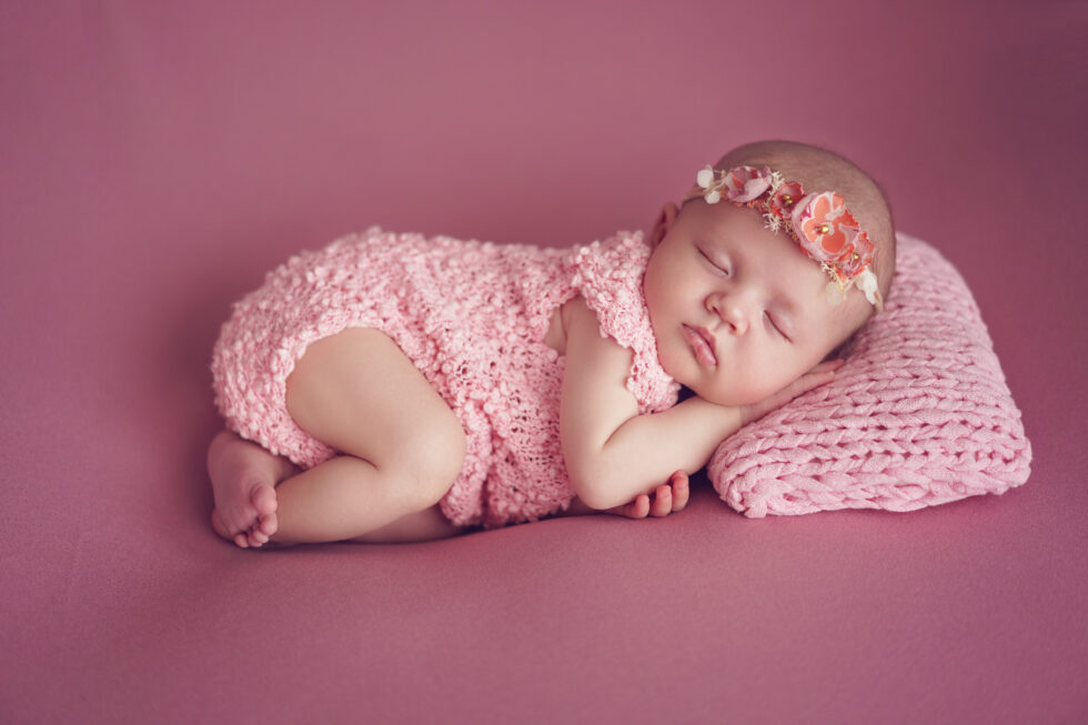 Pasgeboren baby gewikkeld in een roze kanten doek, vredig slapend op een zachte roze deken.