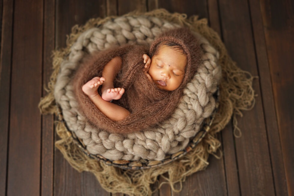 Pasgeboren baby in een bruine gebreide wikkel, opgerold en slapend in een gezellige, rustieke mand.