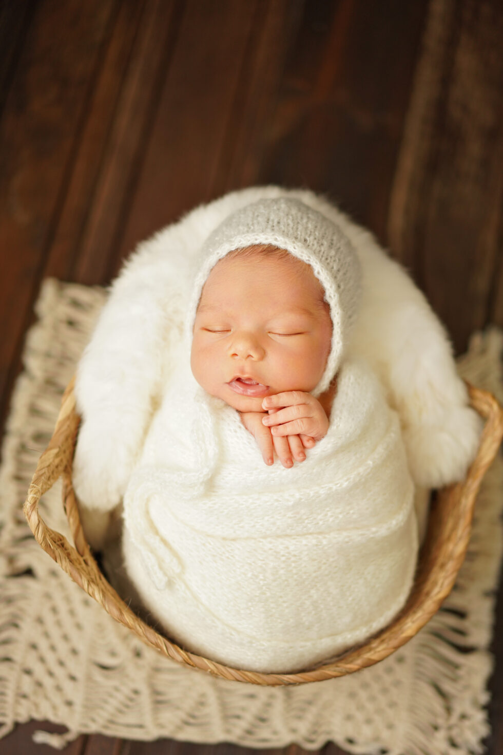 Pasgeboren baby gewikkeld in een witte doek, liggend op een donzig kussen in een rustieke houten schaal
