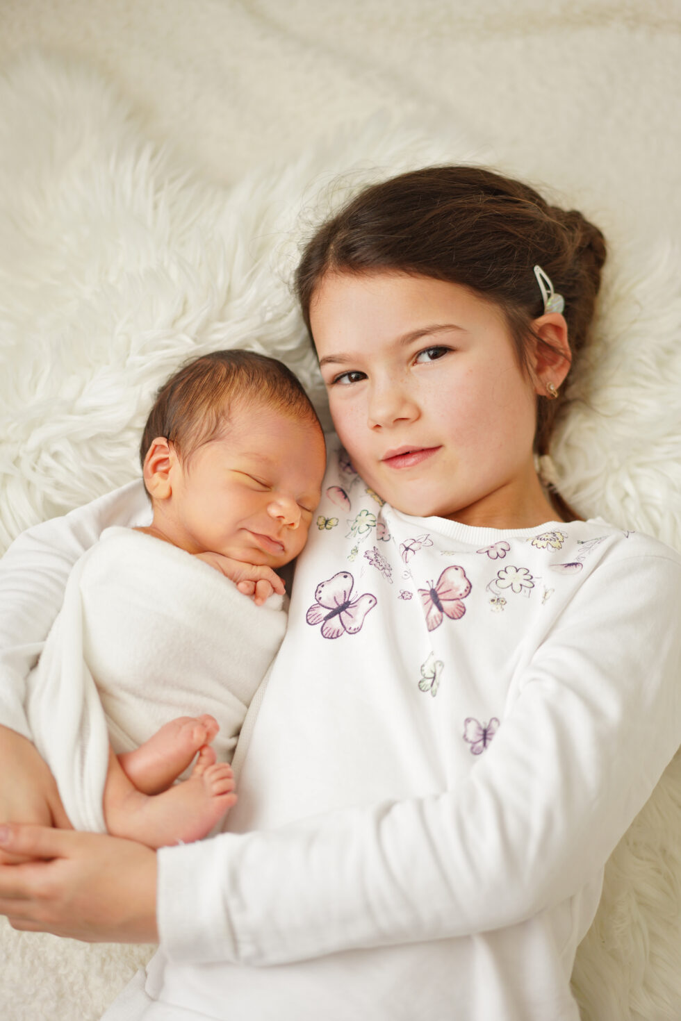 Pasgeboren meisje slapend in een donzige witte deken, met een oudere zus die naar haar glimlacht