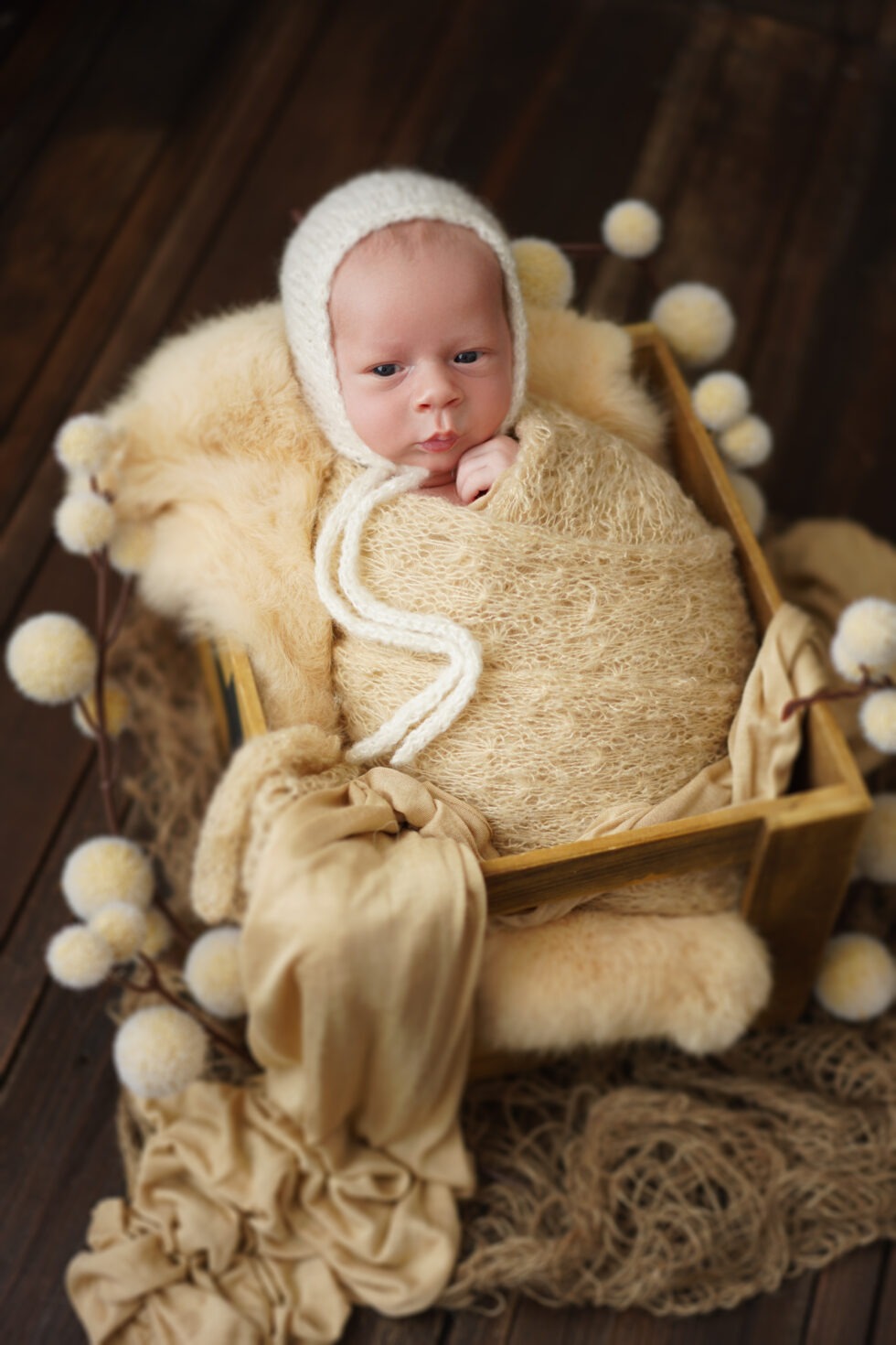 Pasgeboren baby in een gele gebreide outfit met een bijpassende hoed, slapend op zijn zij op een groene deken