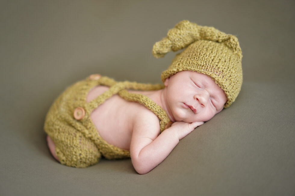 Pasgeboren baby in een gele gebreide outfit met een bijpassende hoed, slapend op zijn zij op een groene deken