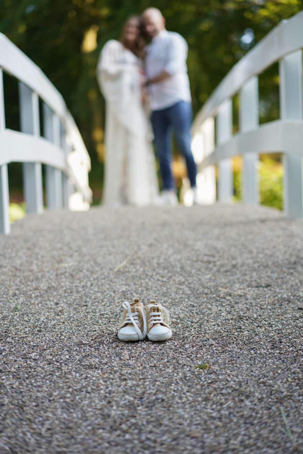 Een close-up van een paar babyschoentjes op een geplaveid pad, met het stel op de achtergrond.