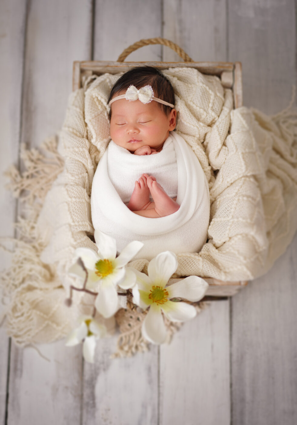 Pasgeboren baby rustend in een halve maanvormige mand, omringd door een paarse en grijze deken.