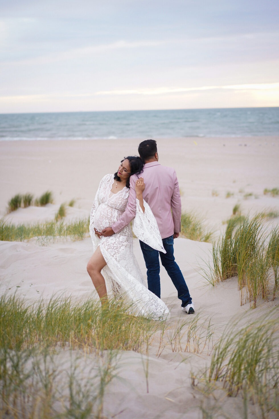 Een stel loopt hand in hand over het strand, met de vrouw in een witte jurk.