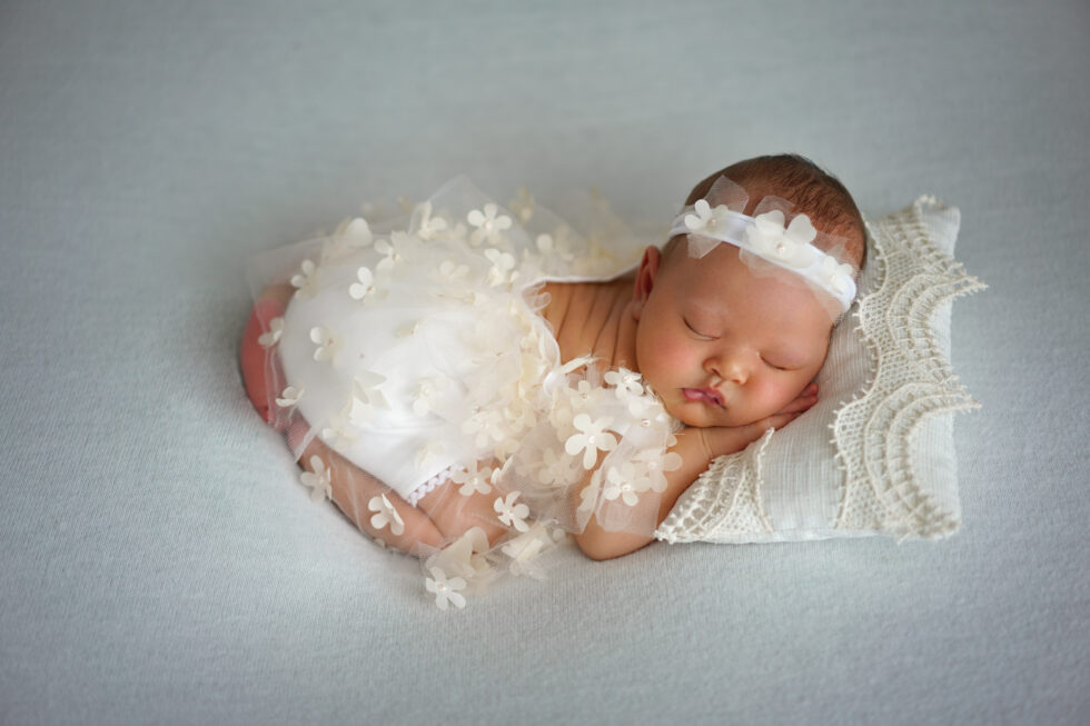Pasgeboren meisje met een witte bloemenhoofdband, slapend op een donzige witte deken