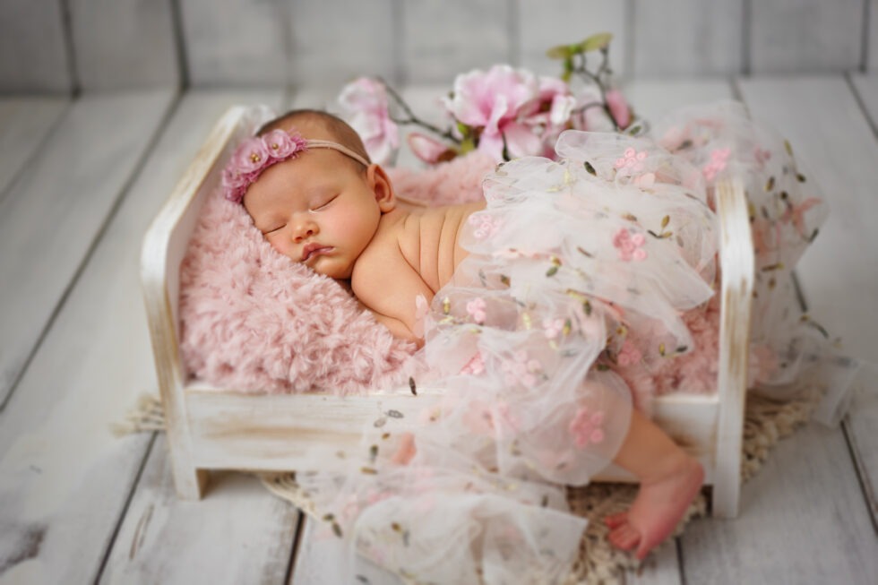 Pasgeboren meisje in een roze tutu, liggend op een zacht kussen, omringd door bloemen en groen.