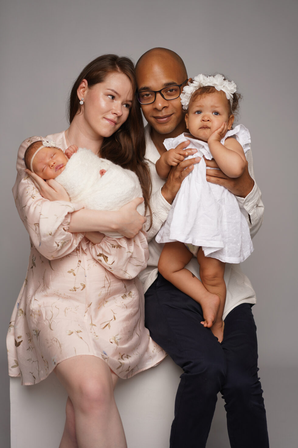 Familieportret met een pasgeboren baby in de armen van beide ouders, allen gekleed in zachte, neutrale tinten.