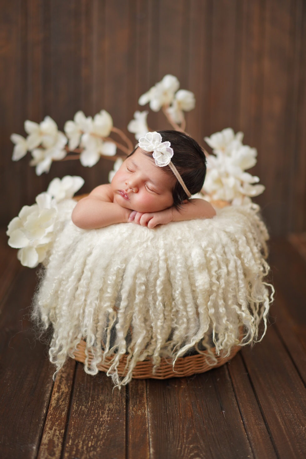 Pasgeboren meisje in een witte outfit en bloemenhoofdband, slapend in een mand bekleed met crèmekleurige vacht